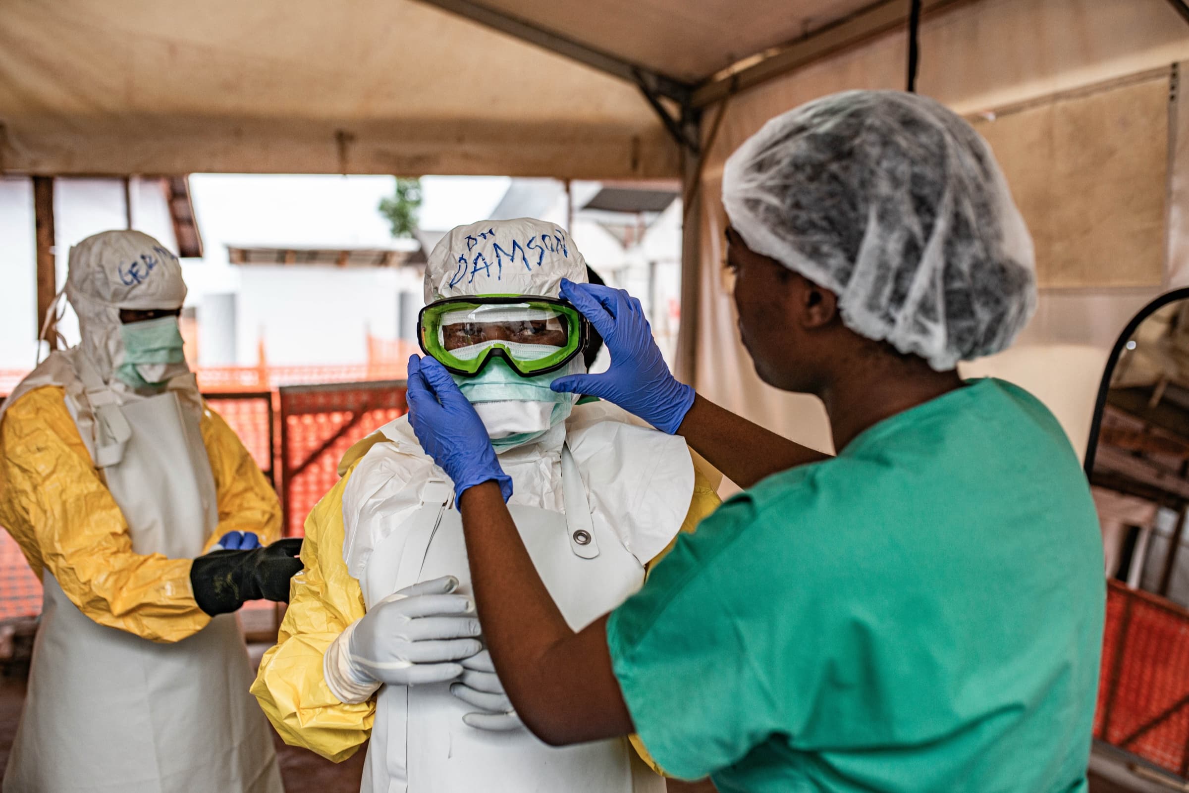 A health worker adjusts a colleague's goggles as they put on protective equipment against Ebola